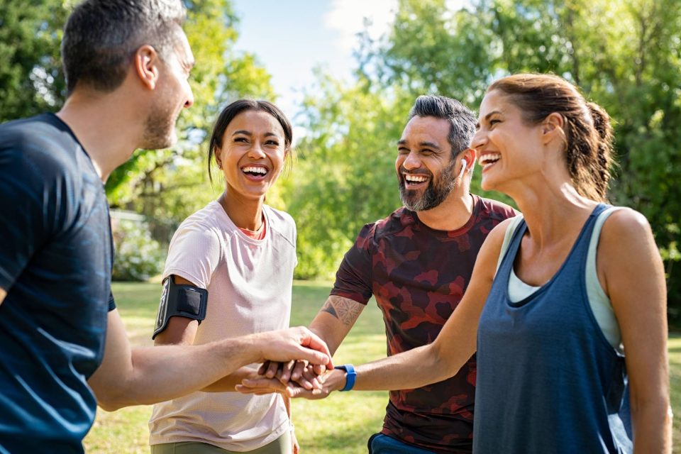 Two men and two women stacking their hands together while wearing exercise clothing preparing for a team event.