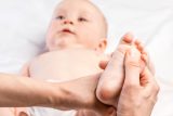 Closeup of adult hands rubbing an infant's feet as part of ongoing pediatric chiropractic care.