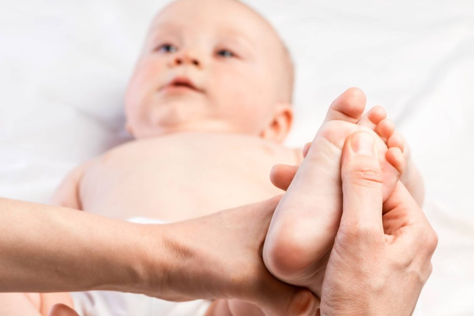 Closeup of adult hands rubbing an infant's feet as part of ongoing pediatric chiropractic care.