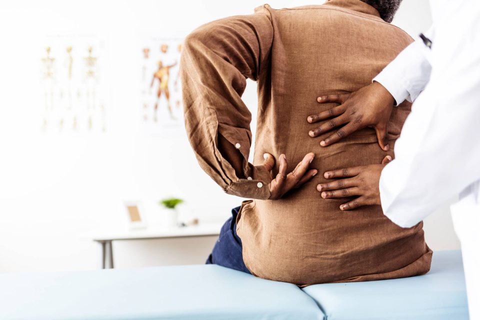 Chiropractor pressing their hands to a patient's back while patient points to where their pain is on their body.