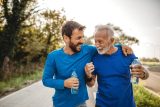 Two Caucasian men running outside together while they smile and hold water bottles.