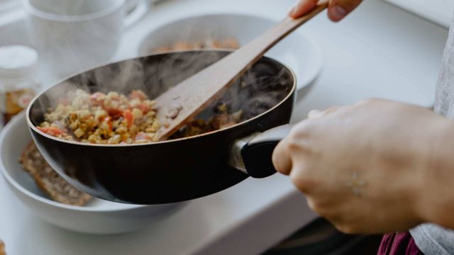 Closeup of hands serving healthy food out of a skillet into bowls with a wooden spatula.