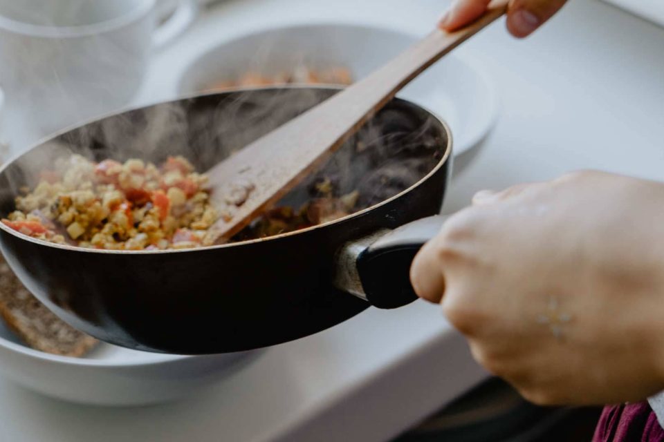 Closeup of hands serving healthy food out of a skillet into bowls with a wooden spatula.