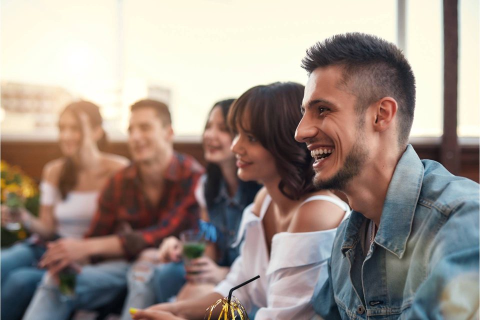 Group of Caucasian young people sitting outside holding drinks and smiling.