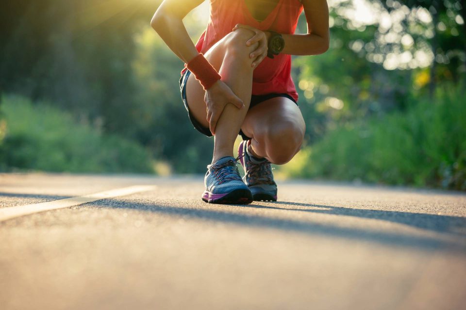 Female runner squatting down on a road, holding their shin and calf due to a sports injury.